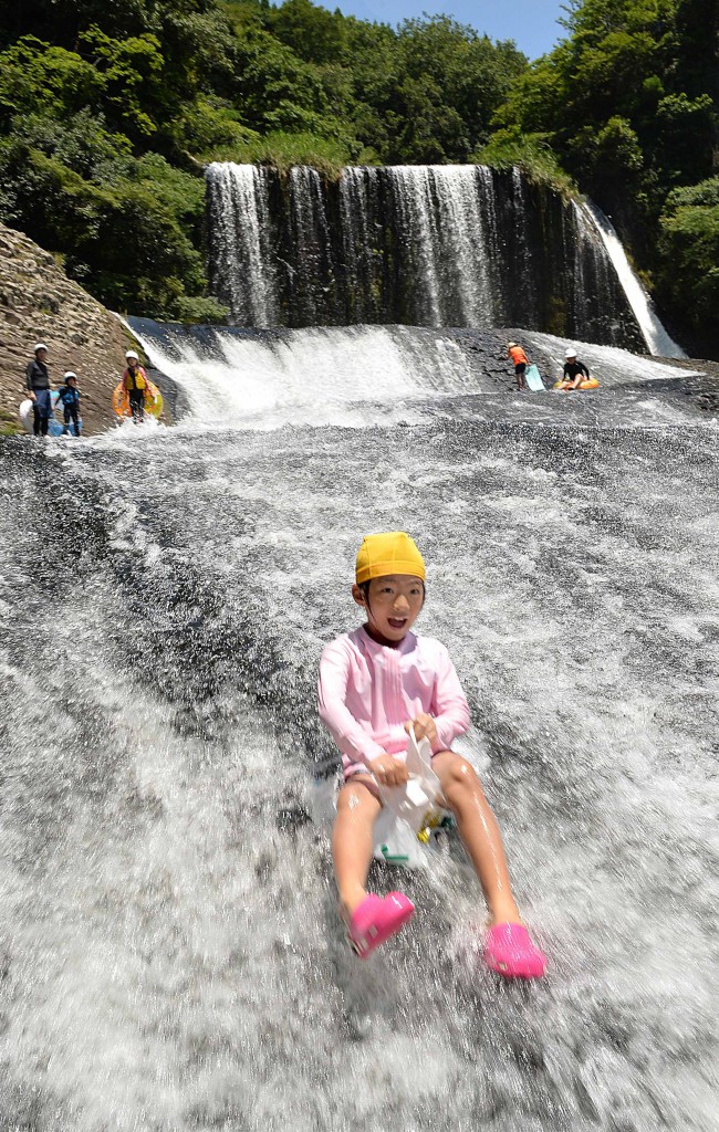 A girl enjoys sliding down the river, sitting on a fertilizer bag, at Ryumon no Taki waterfalls in Kokonoe, Oita Prefecture.