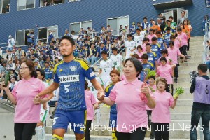 Female members of JA Ochiimabari, an agricultural cooperative in Imabari, Ehime Prefecture, serve as escorts to players of local soccer team FC Imabari at Arigato Service Yume Stadium in the town on June 10.