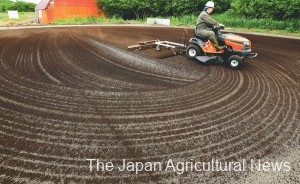 A worker of a local farm coop tows a self-made rake to spread pelletized compost over paved ground for sun-drying in Shimizu, Hokkaido.